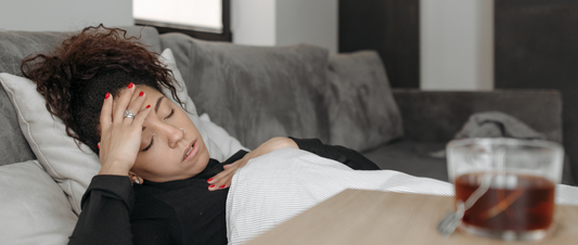 Person lying in dark room with migraine, attempting to sleep Migraine relief tools next to bed for sleep support Woman wishing she was using blackout sleep dento rest during migraine attack