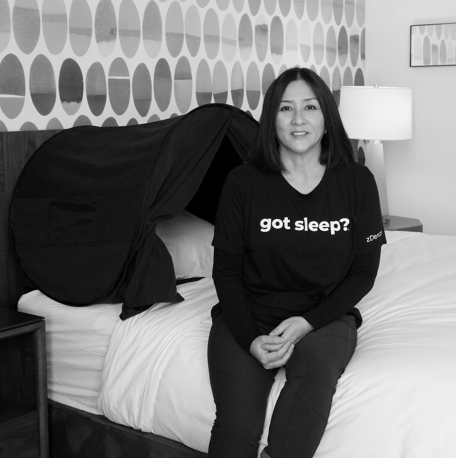 Photo: Danielle Fujii, creator of zDen, next to her light-blocking sleep solution on a bed, wearing a "got sleep?" t-shirt.